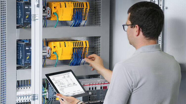 A person inspects the wiring and configuration of safety and automation components in an open control cabinet