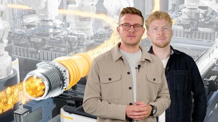 Two people standing in front of a display showing IO-Link Safety and an automated production plant featuring industrial robots and a visualised data stream